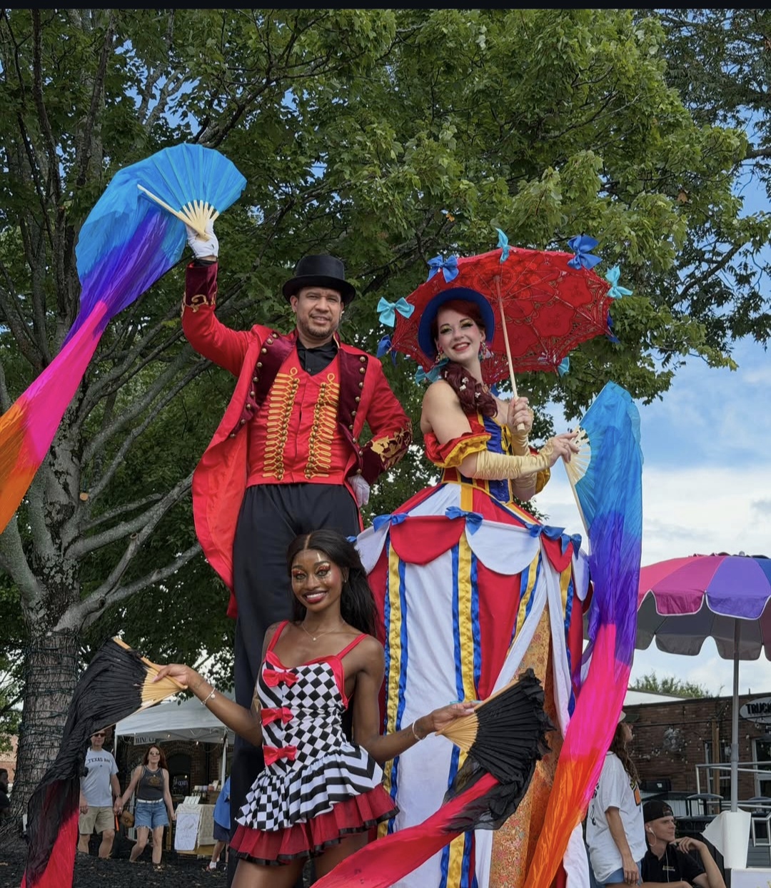 Circus performers on stilts in ringmaster and harlequin costumes at an outdoor event